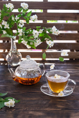 Green jasmine tea in transparent cup with hot steam and jasmine flowers and teapot on wooden table. Copy space. Food levitation