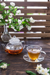 Jasmine tea in transparent cup, jasmine flowers and teapot on wooden table. Copy space. Tea party