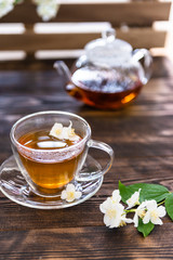 Jasmine tea in transparent cup, jasmine flowers and teapot on wooden table. Copy space. Tea party