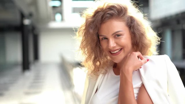Portrait of young atractive curly woman smiling and looking at camera. White dress. Sunlight on hair