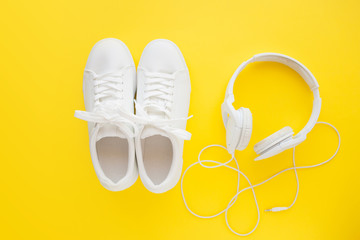 Perfect white new sneakers standing on a bright yellow background near to white headphones.