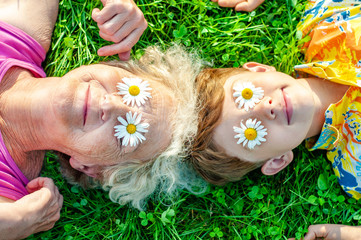 Happy family - grandmother with grandson having fun lying on the lawn with daisies on their eyes....