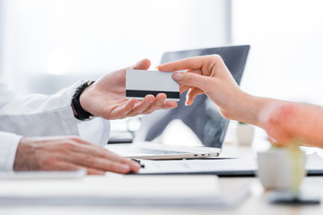 partial view of patient giving credit card to doctor in clinic