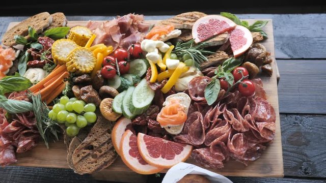 Assorted Ham, Sausage, Mozzarella Cheese, Grapes, Grapefruit, Dates, Basil on a wooden board for a buffet in a restaurant or event 4K