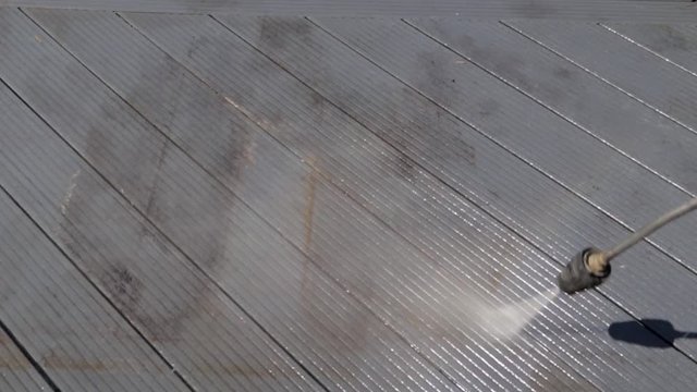 high pressure water jet cleaner washing dirty black deck outside and making a rainbow with the vapor