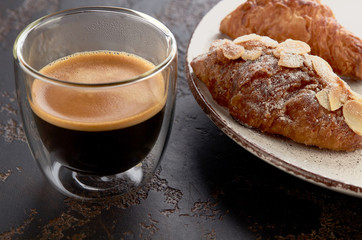 Cup of espresso and an almond croissant on a plate close-up. Delicious breakfast.
