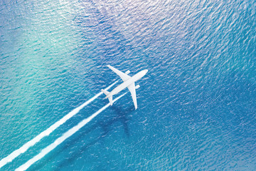 The plane flying over the sea leaves a white trail of smoke, a shadow on the surface of the water.