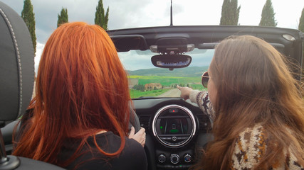 Two women sitting in the cabriolet and riding - a woman pointing at something