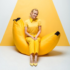cheerful blonde woman sitting on bean bag chair on white and yellow
