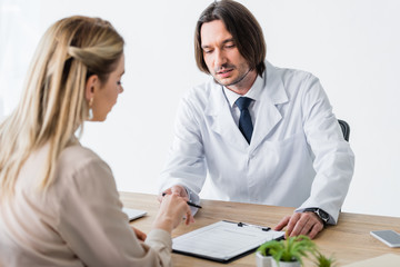 patient sitting with doctor behind wooden table and signing document