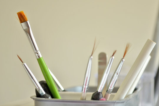 Brushes and tools for manicure and nail art in a white glass in the beauty salon on the background of a wall