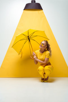 happy blonde girl holding umbrella while sitting on white and yellow