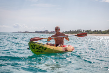 Elder fit man is kayaking on a bright yellow kayak in Caribbean Sea during a sunny summer day. Taken in Varadero, Cuba.