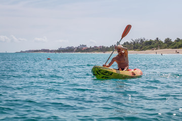 Elder fit man is kayaking on a bright yellow kayak in Caribbean Sea during a sunny summer day. Taken in Varadero, Cuba.