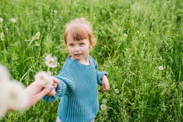 Mother and the little daughter play on a green meadow with dandelions.