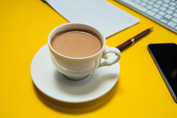 A modern office with a computer, a smartphone with a black screen on a laptop and a cup of coffee. Top view with a copy, keyboard and camera for headphones. isolated on a yellow background
