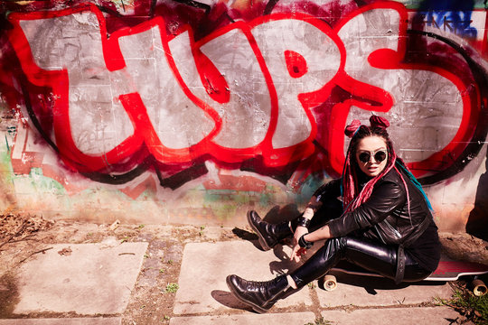 Stylish girl with dreadlocks photographed near graffiti