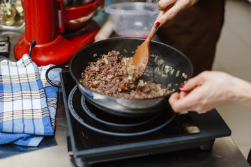 The chef roasts the mince in a deep pan. Ready stuffing with onions in a bowl on the background of spices and greens.