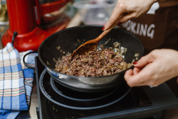 The chef roasts the mince in a deep pan. Ready stuffing with onions in a bowl on the background of spices and greens.