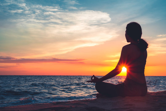 Silhouette young woman practicing yoga on the beach at sunset.