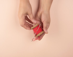 two hands hold a wooden bobbin with red wool threads