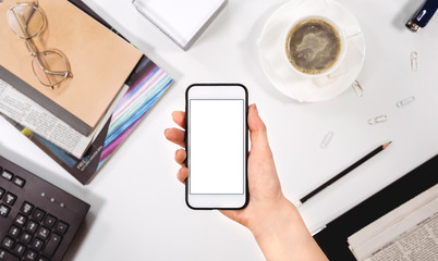 The girl holds the phone in her hands, white screen. Against the background of the desktop, office background. Copy space