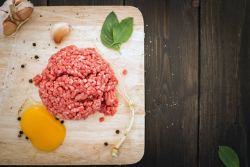 Minced beef on a cutting board and egg york with spice on wooden background