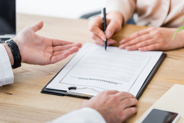 cropped view of woman signing insurance claim form near doctor in clinic
