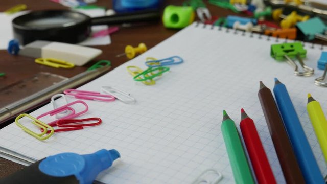 Multicolored Pencils, Paper Clips and Notebook on Brown Wooden Desk. School Office Supplies on brown wooden table. Concept of back to school