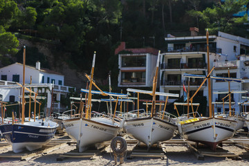 Fototapeta na wymiar Traditional fishing boats standing in the shore. Small fisherman's village in Catalonia, Spain. Wooden boats on the bay, Mediterranean sea. White buildings are on the background. Summer vacations