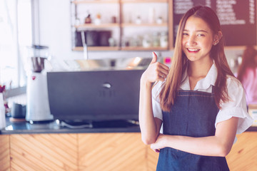 Pretty young asian waitress standing arms crossed in cafeteria.Coffee Business owner Concept.  barista in apron smiling at camera in coffee shop counter