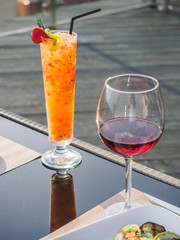 Tropic orange cocktail with glass of red wine on the table