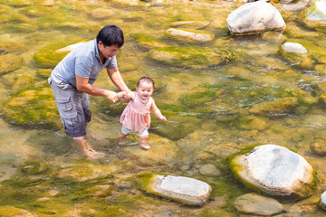 Man holding his baby daughter walking in shallow water