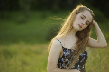 Fototapeta premium beautiful young blonde with long flowing hair on a blurred background of summer greenery