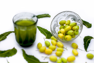 Detox or detoxifying drink of neem fruit in a glass isolated on white along with some neem fruit or nimbodi or nimbudi in a glass bowl.