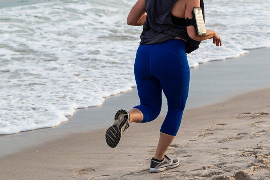 Women running along the shore with cell phone strapped on arm