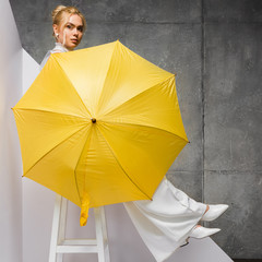 beautiful girl sitting on chair and holding yellow umbrella on white and grey