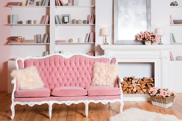 Modern light interior with fireplace, spring flowers and cozy pink sofa