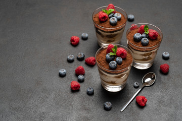 Classic tiramisu dessert with blueberries and raspberries in a glass on dark concrete background