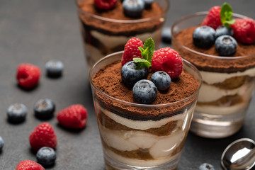 Classic tiramisu dessert with blueberries and raspberries in a glass on dark concrete background