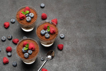 Classic tiramisu dessert with blueberries and raspberries in a glass on dark concrete background