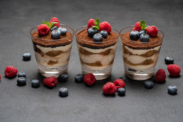 Classic tiramisu dessert with blueberries and raspberries in a glass on dark concrete background