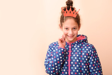 A portrait adorable little girl with princess crown red paper mask at kids birthday party or Purim or fool day or Halloween. Copy space. Suitable for greeting card, invitation, proposing product.