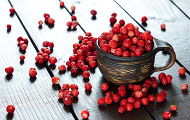 Wild strawberry in an earthen cup with ornament on wooden table with forest berry laying around, closeup, copy space, healthy food and vegetarian eating concept
