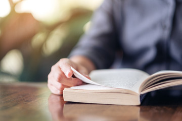 Closeup image of a woman holding and reading a vintage novel book on wooden table