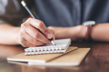 Closeup image of a woman writing on blank notebook on wooden table