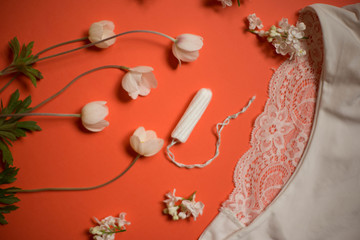 White lace panties with tampon on a coral background. Female underwear for the bride with delicate flowers on an orange background.