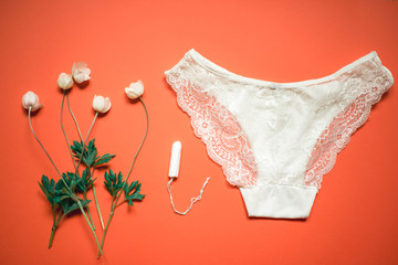 White lace panties with tampon on a coral background. Female underwear for the bride with delicate flowers on an orange background.