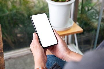 Mockup image of a woman holding and using black mobile phone with blank desktop screen in cafe