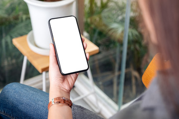 Mockup image of a woman holding and using black mobile phone with blank desktop screen in cafe